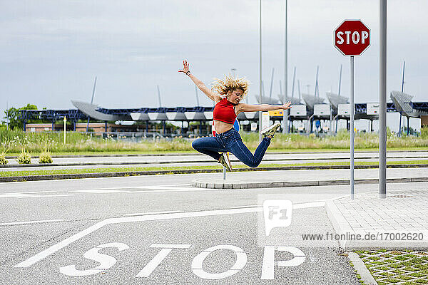 Junge Frau springt in der Luft über ein Stoppschild auf der Straße