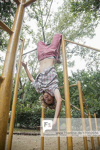 Boy taking selfie while hanging upside down on outdoor play equipment in park