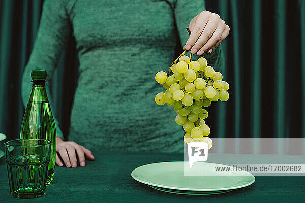 Midsection of woman holding grapes fruit while standing against green curtain