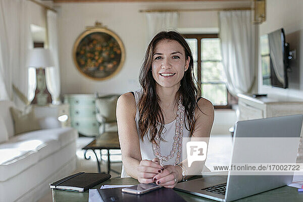 Smiling female event planner sitting by laptop at home