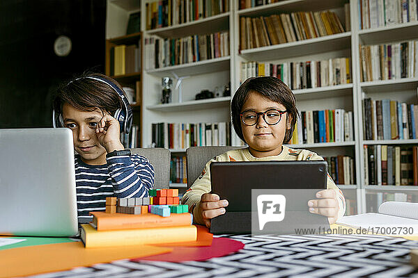 Lächelnder Junge beim E-Learning am Laptop  während ein männlicher Freund zu Hause zuschaut