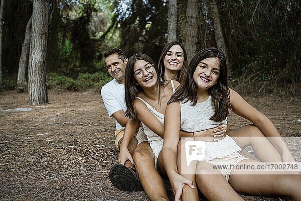Lächelnde Familie in Reihe sitzend im Wald im Urlaub