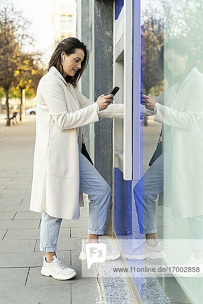 Stilvolle Unternehmerin  die ein Smartphone benutzt  während sie Geld vom Geldautomaten abhebt