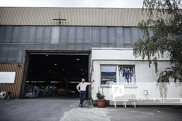 Männlicher Unternehmer  der sich an eine Kabine lehnt  während er am Eingang der Fabrik steht