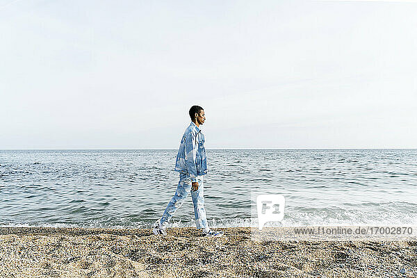 Junger Mann in Jeans-Outfit läuft gegen das Meer