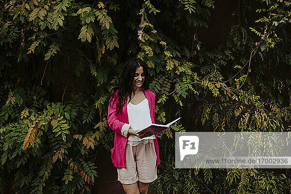Unternehmerin liest Tagebuch  während sie an einem Baum steht