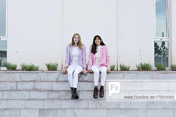Happy sisters sitting on retaining wall
