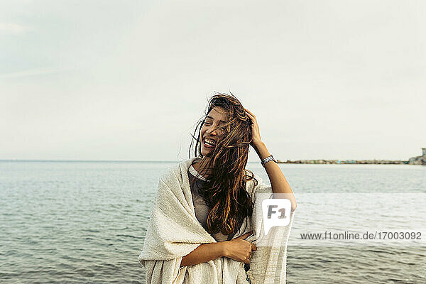 Frau mit Hand in den Haaren  die lachend am Strand am Meer steht