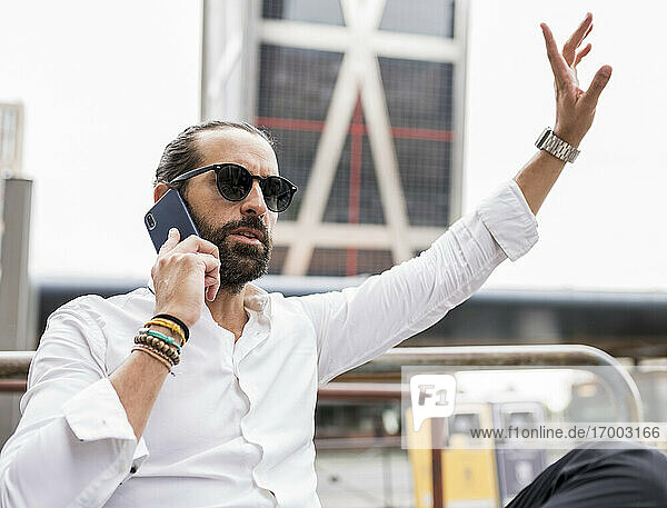 Portrait of bearded businessman wearing sunglasses waving while talking on smart phone