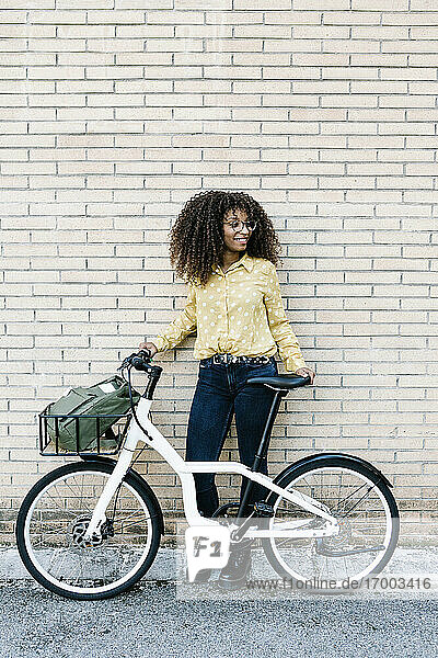 Young woman standing with bicycle against brick wall