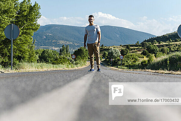 Young man standing in middle of road on sunny day