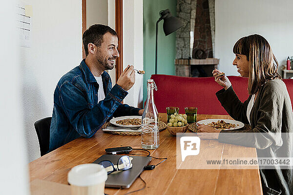 Smiling business couple eating food at table in living room at home