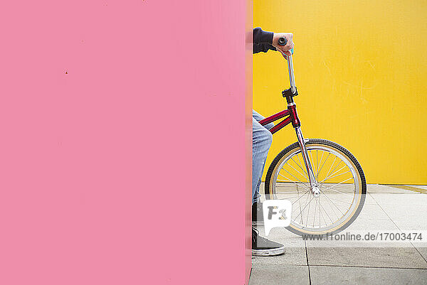 Teenage boy on BMX bike hiding behind pink wall