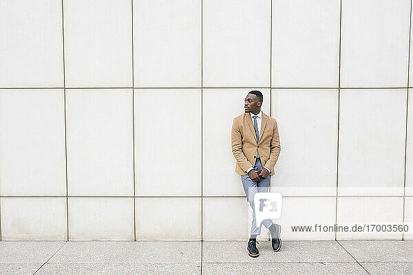 Young businessman leaning against a wall looking sideways