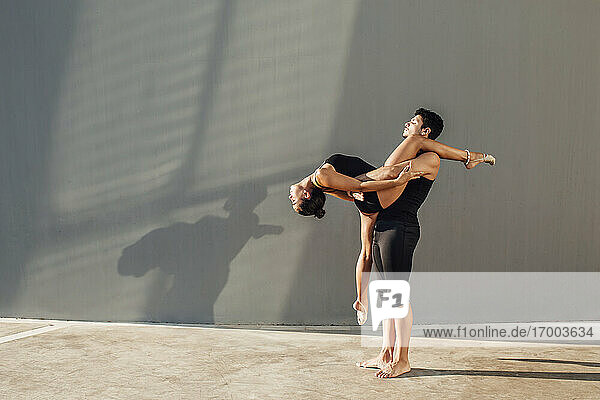 Junger Mann hilft flexible Frau tun Tanz Pose gegen die Wand