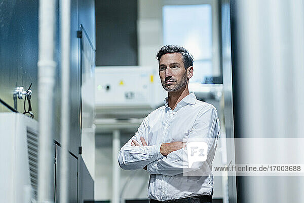 Mature businessman with arms crossed looking away while standing in factory