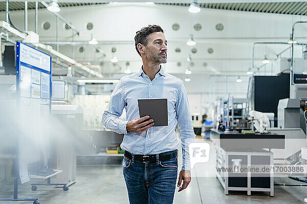 Geschäftsmann hält digitales Tablet beim Gehen in der Industrie