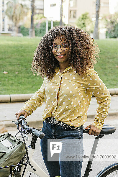 Lockenköpfige Frau mit Fahrrad auf der Straße stehend