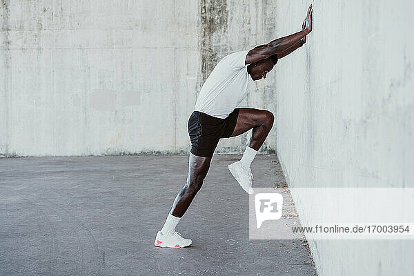 Sportsman doing stretching workout while leaning on white wall