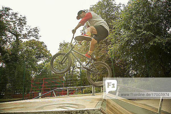 Junger männlicher BMX-Fahrer  der einen Stunt in der Luft im Skateboard-Park vollführt