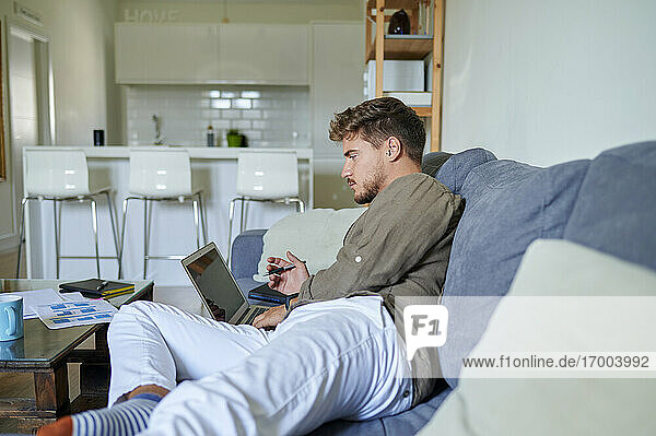 Geschäftsmann  der einen Laptop benutzt  während er zu Hause auf dem Sofa liegt