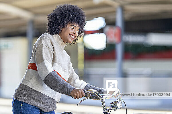 Lächelnde junge Frau mit Fahrrad wartet am Bahnhof