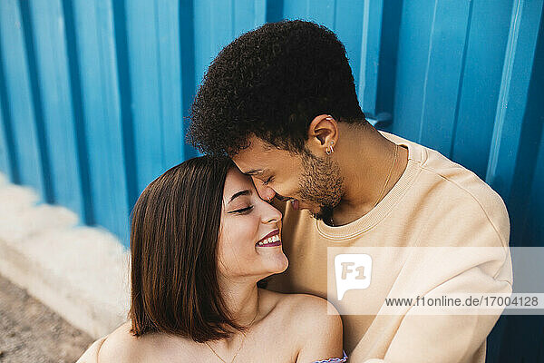 Lächelndes junges Paar sitzt von Angesicht zu Angesicht an einer blauen Wand