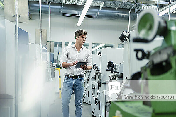 Businessman with digital tablet walking in factory while examining machinery equipment