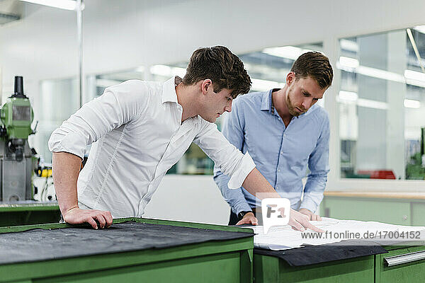 Male colleagues discussing over blueprint in factory