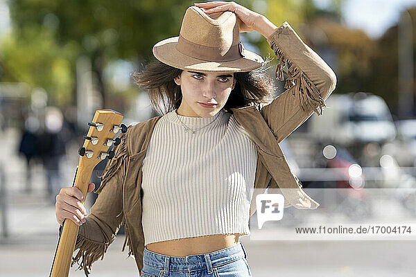 Junge Frau mit Hut und Gitarre in der Hand an einem sonnigen Tag