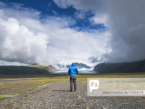 Mann auf unbefestigtem Weg vor dramatischem Himmel am Svinafellsjokull  Island