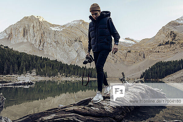 Professioneller Fotograf beim Gehen auf einem Baumstamm am See Ibon Del Plan vor den Bergen  Huesca  Spanien