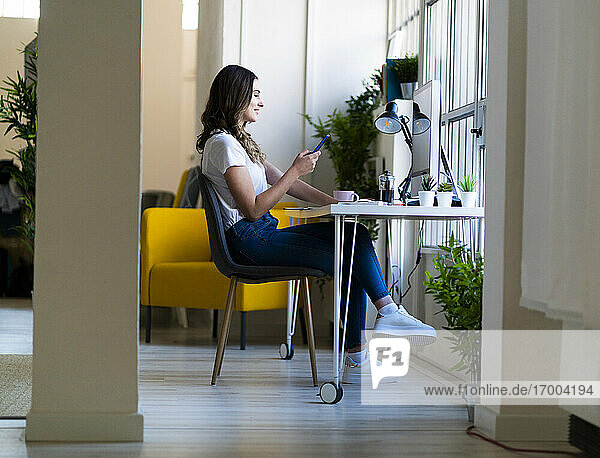Junge Geschäftsfrau  die im Büro sitzend ein Smartphone benutzt