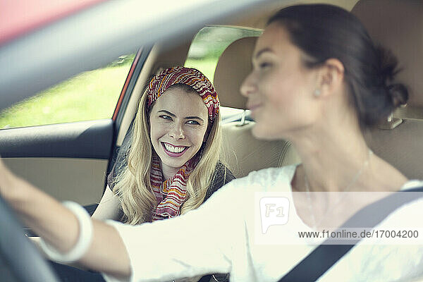 Smiling friends talking while riding in car on road trip