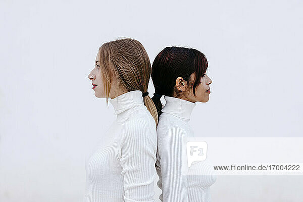 Freundinnen in Rollkragenpullovern stehen Rücken an Rücken vor weißem Hintergrund