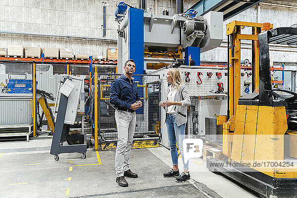Businesswoman discussing with male colleague while standing in factory