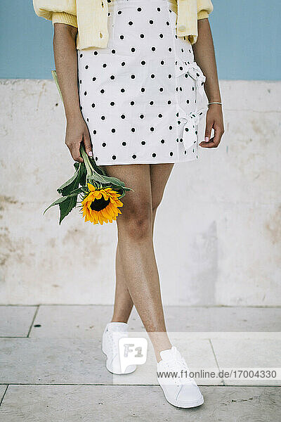 Junge Frau in gepunktetem Kleid hält Sonnenblume  tiefer Ausschnitt