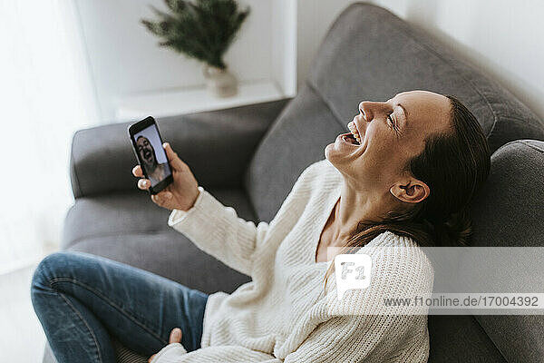 Frau lacht während eines Videogesprächs mit einem männlichen Freund im heimischen Wohnzimmer