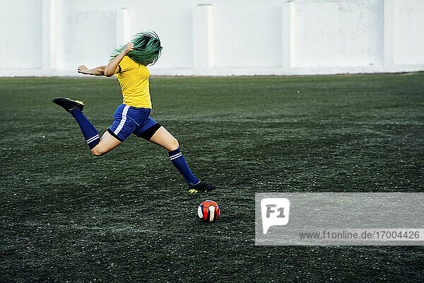 Junge Frau spielt Fußball auf einem Fußballplatz und schießt den Ball