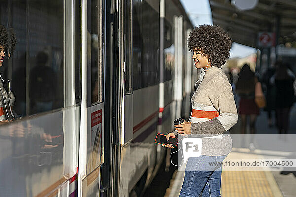 Happy young female passenger boarding train at station on sunny day