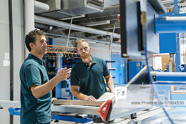 Zwei männliche Schreiner arbeiten zusammen neben einer Kreissäge in einer Produktionshalle