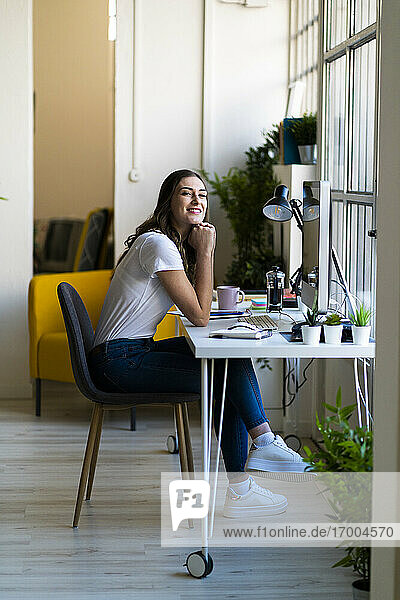 Junge Geschäftsfrau mit Hand am Kinn im Büro sitzend