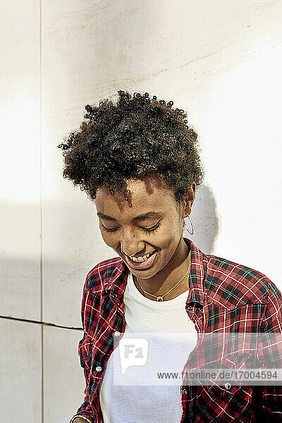 Smiling young Afro female hipster looking down against white wall