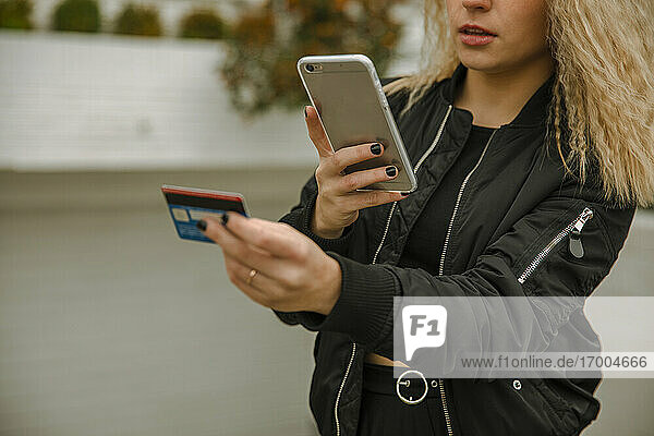 Blonde Frau beim Online-Shopping mit dem Smartphone  während sie mit der Kreditkarte bezahlt