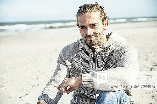 Smiling man sitting with hand on knee at beach
