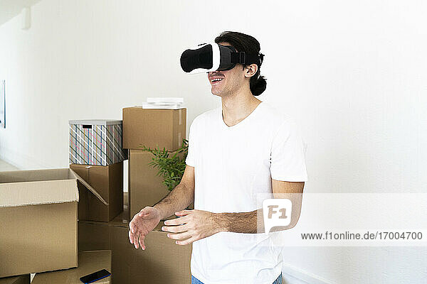 Lächelnder junger Mann mit Virtual-Reality-Simulator in neuer Wohnung