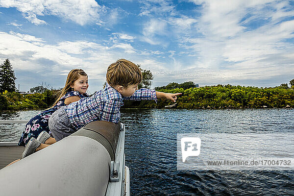 Boy pointing while enjoying with sister in boat on lake against sky