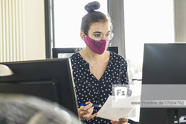 Geschäftsfrau mit Gesichtsmaske bei der Arbeit am Computer  während sie im Büro sitzt