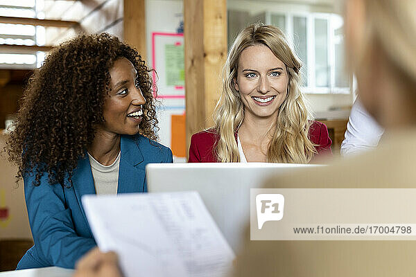 Smiling businesswoman with laptop working with colleagues in meeting at office