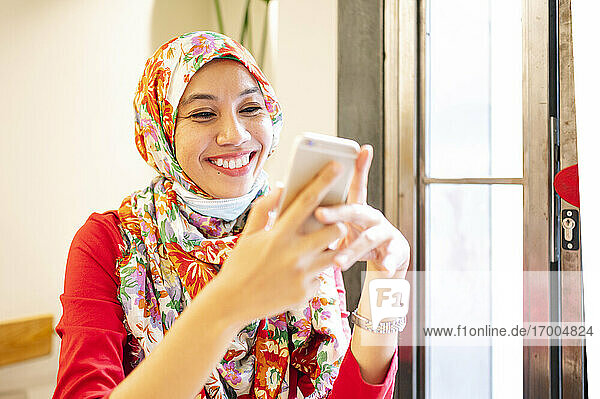 Happy Malaysian woman wearing hijab using smart phone in cafe